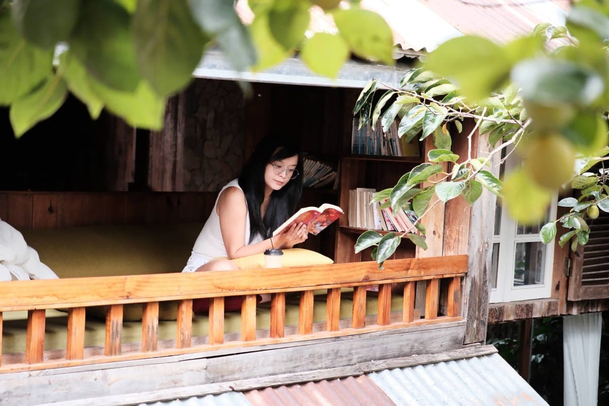Ms. Hiếu Ngô ngồi đọc sách trong một góc nhà gỗ