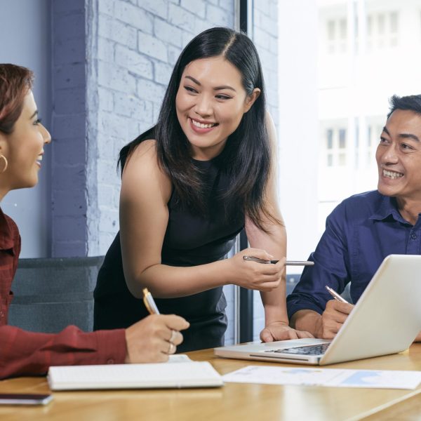 Smiling Vietnamese businesswoman discussing presentations on laptop screen with colleagues